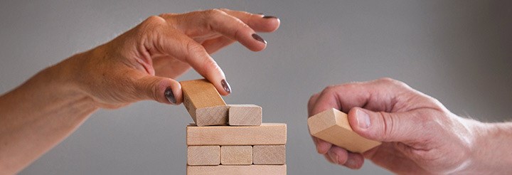 A female and a male hand build a tower of bricks. There is a British flag in the right corner.