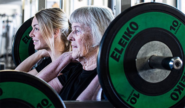 Bilden visar en ung och en äldre kvinna som styrketränar.