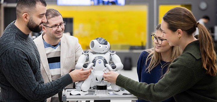 Tre studenter, en lärare interagerar med en robot.