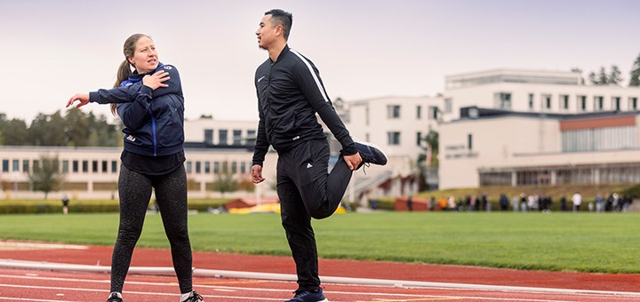 Två sportklädda studenter stretchar.