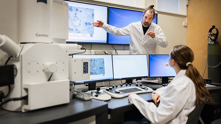 En lärare undervisar en elev framför flera datorskärmar.