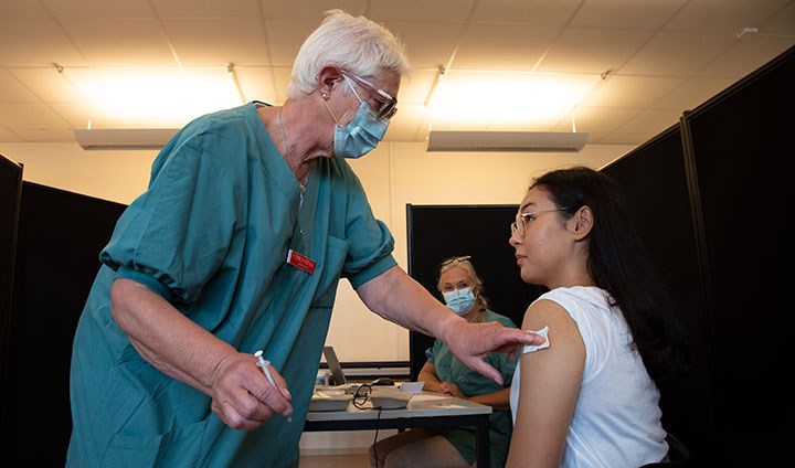 En sjukssköterska sätter plåster efter att ha vaccinerat en student i armen.