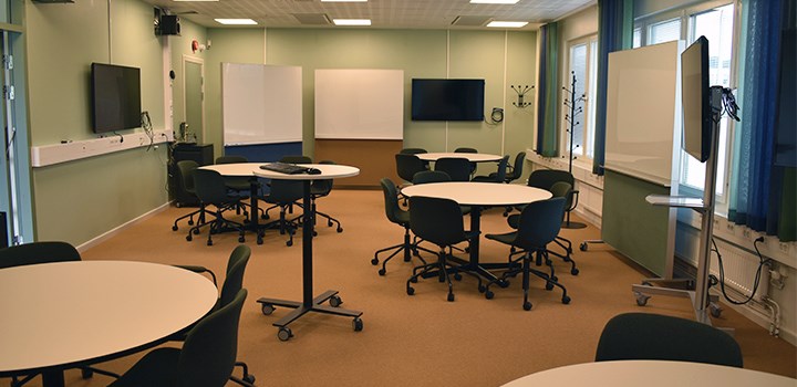 A photo of hall U1191 with 4 round tables chairs and whiteboards