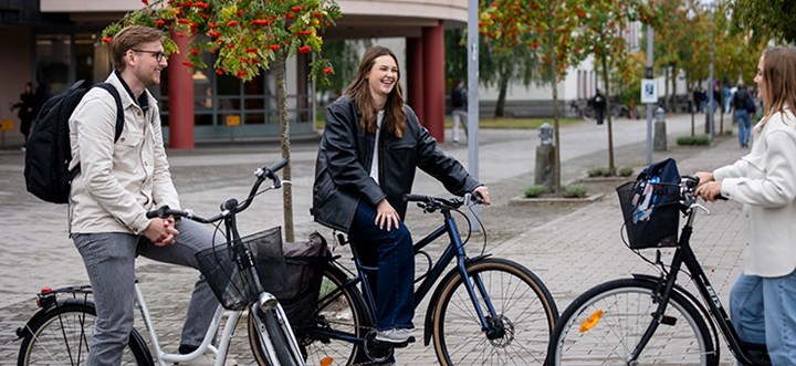Tre studenter med cyklar står utanför biblioteket.