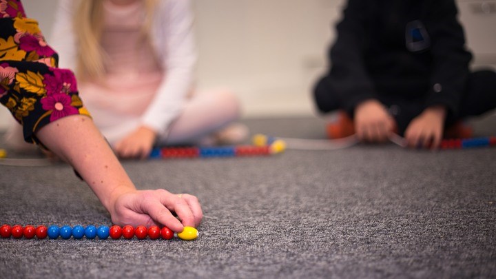 Children sitting on a rug and lining up colorful beads - link to Mathematical Thinking and Learning