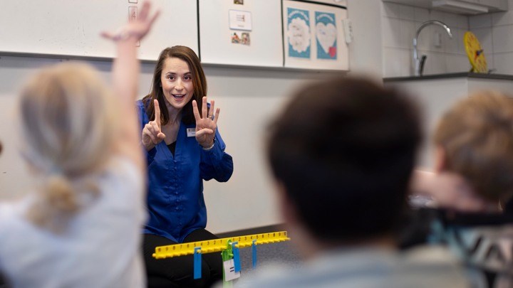 A teacher and a student raising their hands in the classroom - Link to Research on Mathematics Teacher Education and Professional Development