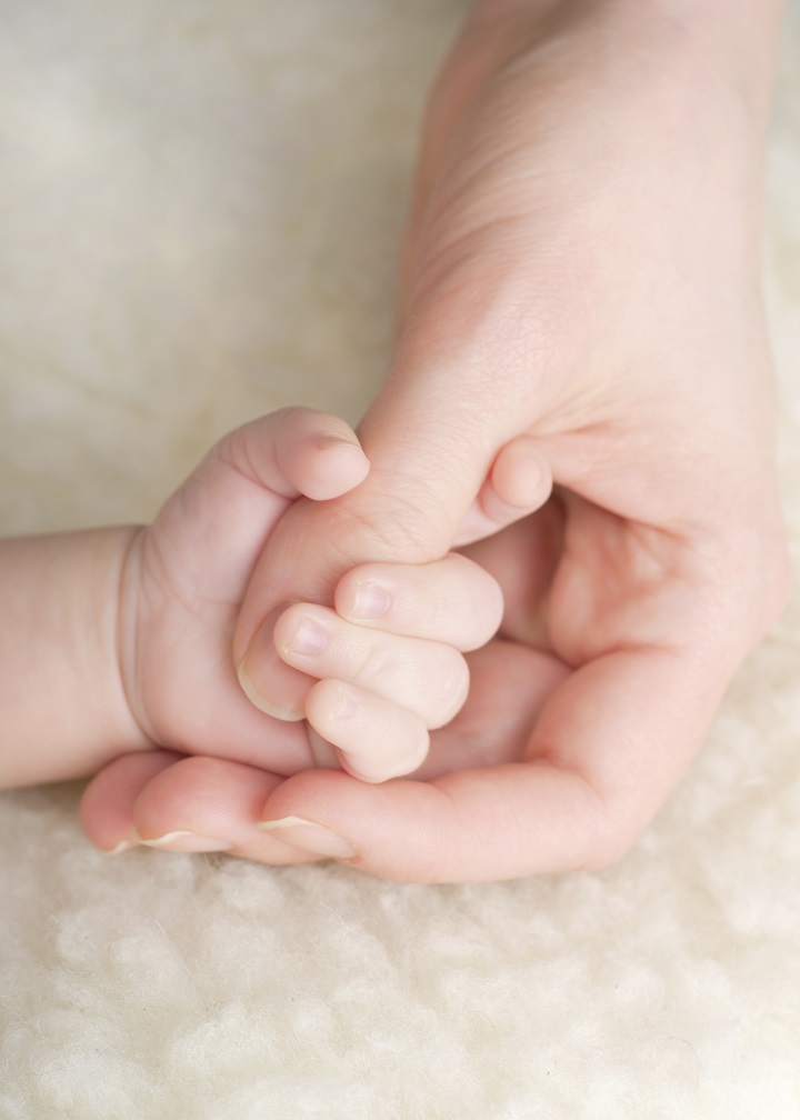 A babys hand wraped around an adult thumb.