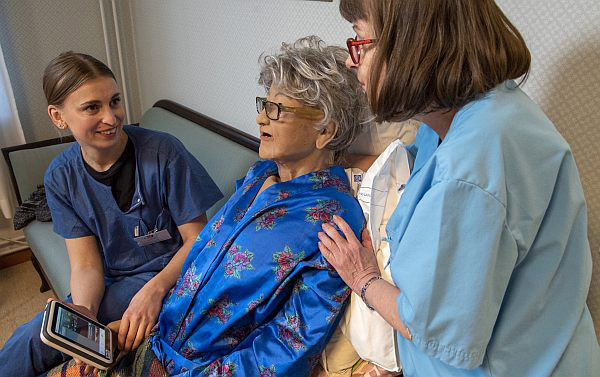 Two healthcare professionals display information on tablet for a life-size doll of an elderly person