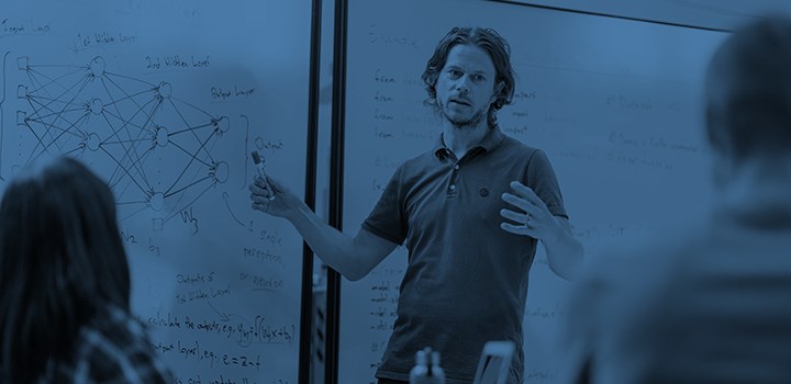 A man talks in front of a white board.