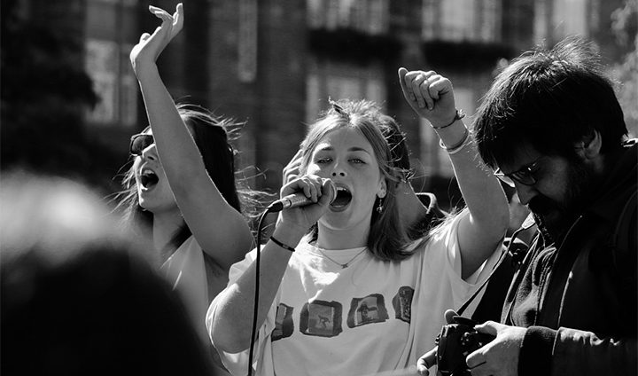 A young girl speaking in a microphone with her arm high in the air.