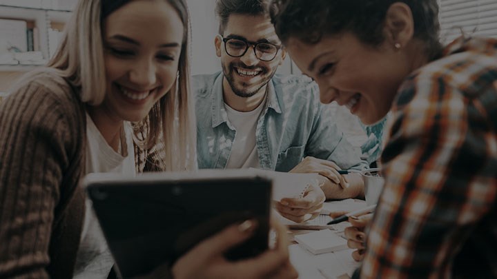 Three happy people looking at a tablet.