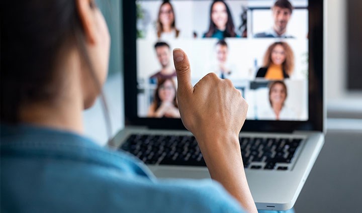 One person shows thumbs up in front of a screen with other people.