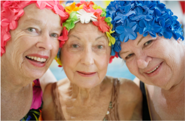 Bilden visar tre damer med färglada badmössor. De ser glada ut. 