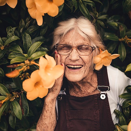 Laughing elderly lady with flowers in garden.