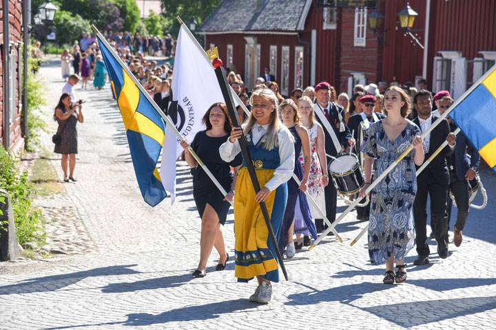 Studenter i ett examenståg går genom gatorna och vajar med Örebro universitetsflaggor.