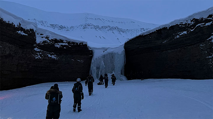 A group of students walking through a wide passage towards a glacier and a snowy mountain in the distance.