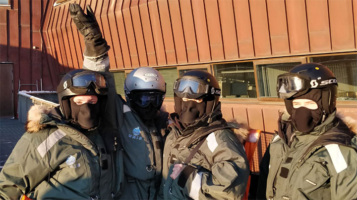 Four students wearing snowmobile overalls and helmets.