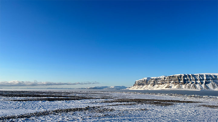 A blue sky over the tree-less tundra with mountains in the background.
