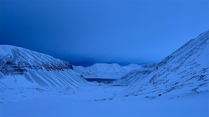 View from Longyearbyen over the night blue sky above snow-covered mountains and a valley.