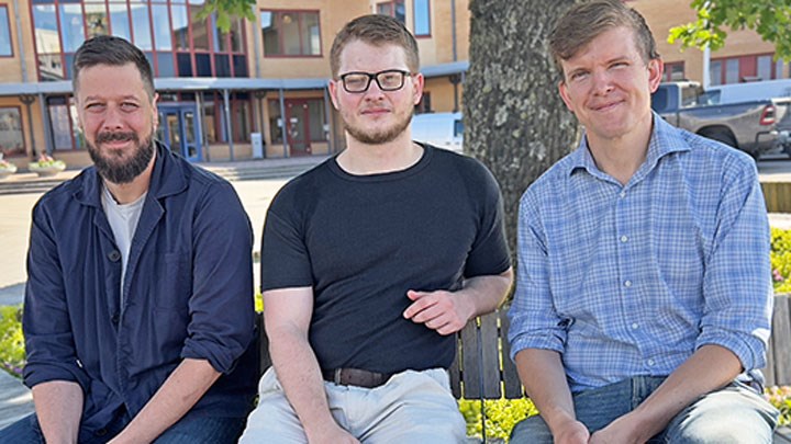 Tre personer sittande på en bänk utomhus.