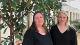 Två kvinnor framför en stor krukväxt inomhus