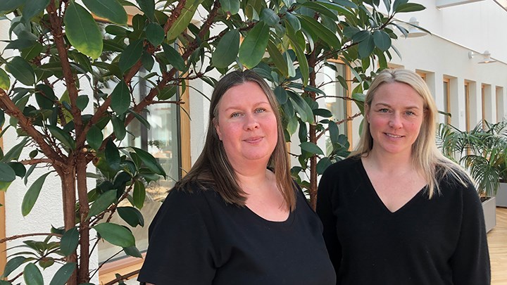 Två kvinnor framför en stor krukväxt inomhus