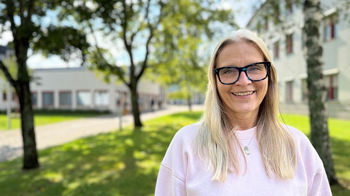 Kvinna i rosa tröja och glasögon framför gräsmatta med träd