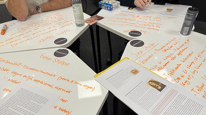 Five desks that double as whiteboards, with writing on them by students.