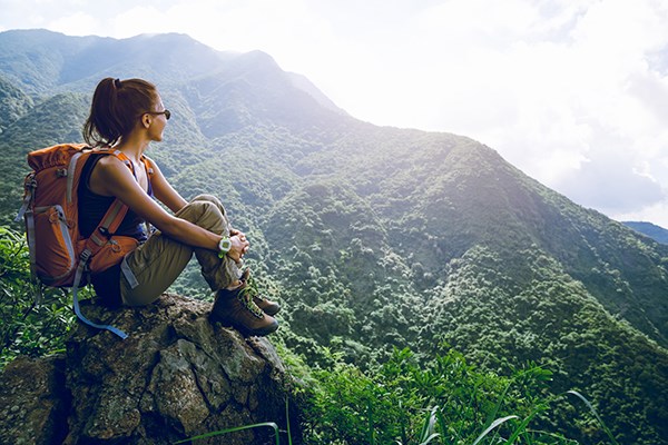 Kvinna med ryggsäck tittar ut över berg och skog