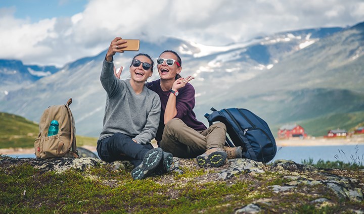 Två studenter tar en gemensam selfie i naturen med vackert berglandskap i bakgrunden