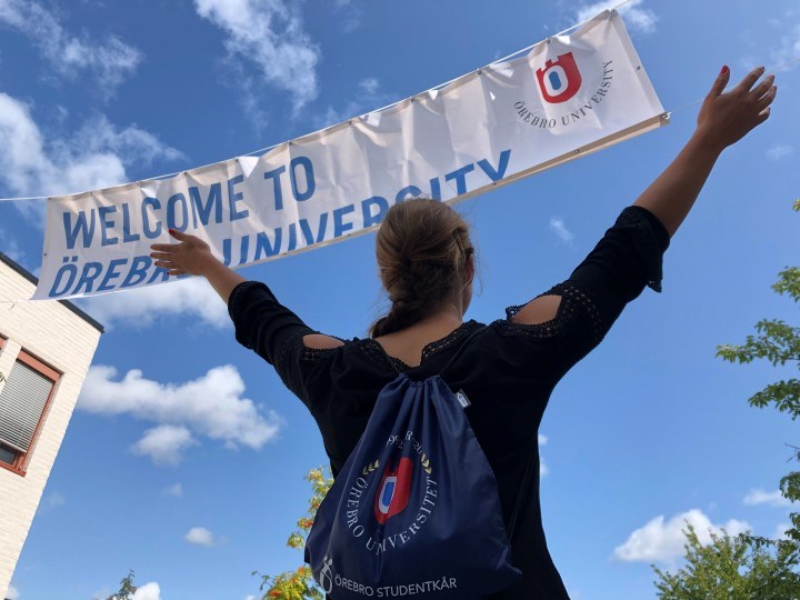 Student som står med ryggen mot och håller upp armarna mot banderollen  "Welcome to Örebro University"