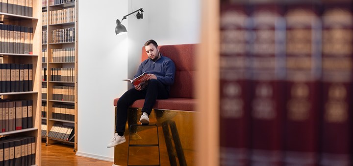 En student sitter och läser i en soffa på biblioteket.