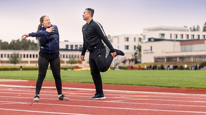 Två personer stretchar på löparbanorna på Campus.