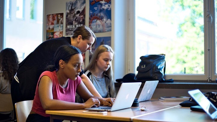 Elever i klassrum vid datorer och lärare hjälper
