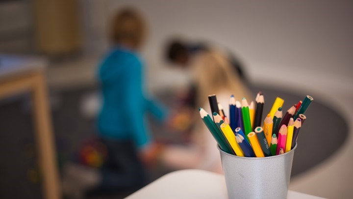 Färgpennor i burk och barn som leker på matta i bakgrunden