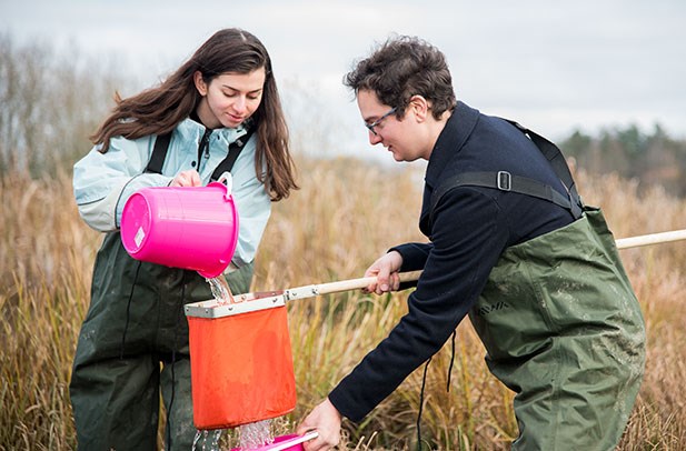 Two people standing outdoor, one pouring water from a bucket.