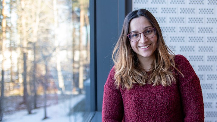 Christina Prevazi står vid ett fönster, hon ler och har en vinröd tröja på sig.