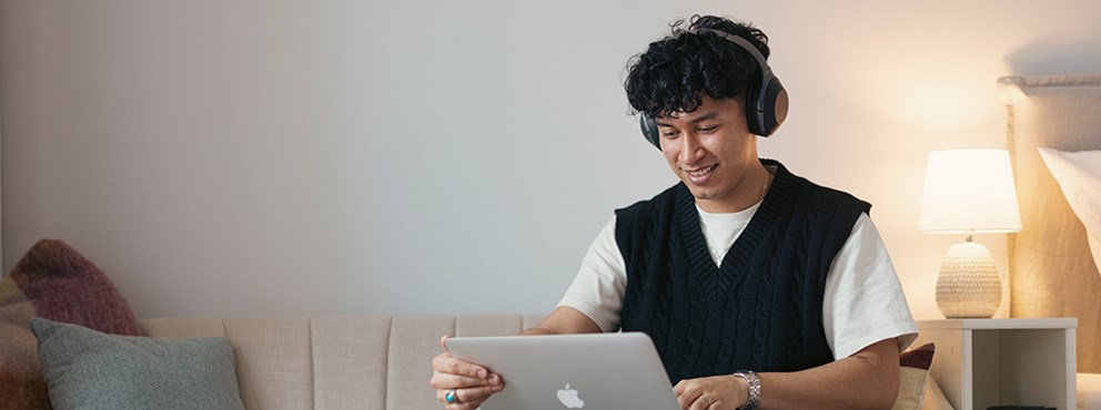 En student sitter i soffan med en laptop i knät.