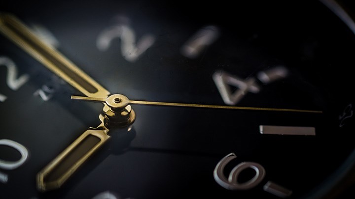 Närbild på en klocka med svart urtavla och guldiga visare.