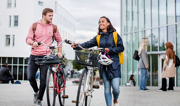 Två studenter som går med sina cyklar på campus.