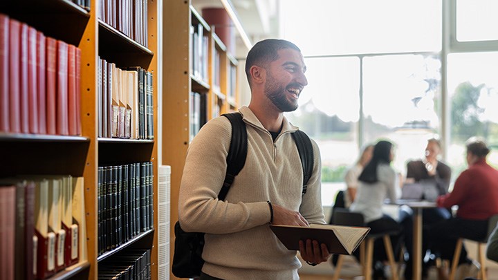 En manlig student är glad och läser en bok i biblioteket.