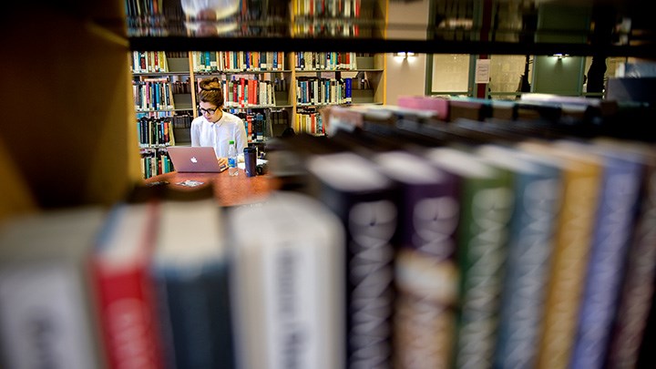 Foto på en person som sitter omringad av bokhyllor vid en dator