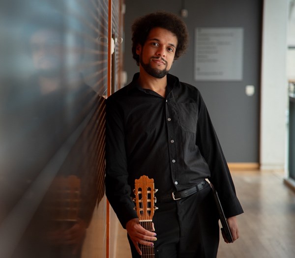 En person som lutar sig mot en vägg och håller en gitarr, med en spegelbild på väggen.